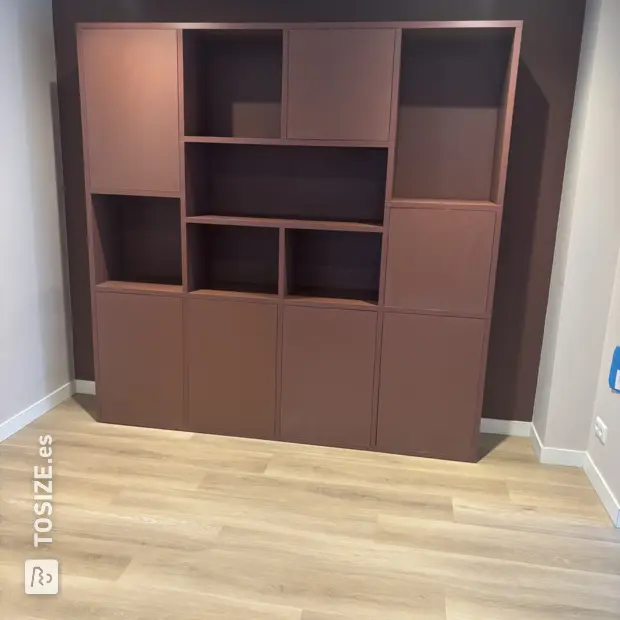 Armario de pared rojo con compartimentos y puertas abiertas.
